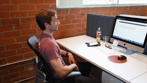 A young man sitting in an office chair at a desk with a computer, exhibiting poor posture, highlighting the issue of a non-ergonomic workspace.