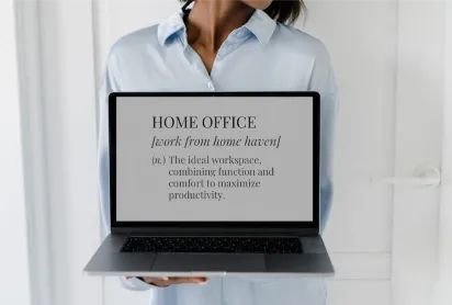 A person in a light blue shirt holding a laptop that displays the text "HOME OFFICE [work from home haven] (n.) The ideal workspace, combining function and comfort to maximize productivity."