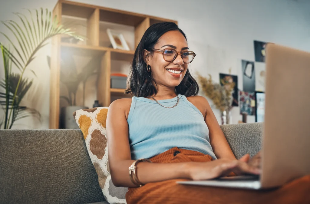 Smiling woman with glasses sitting on a couch using a laptop