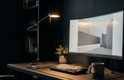 Clean minimal home office desk with architect-style desk lamp illuminating keyboard and monitor, warm light