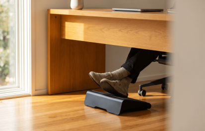 Clean minimal home office desk with ergonomic footrest under a wooden desk in warm natural light