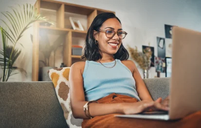 Smiling woman with glasses sitting on a couch using a laptop